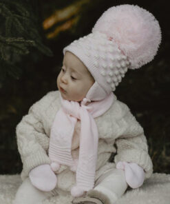Baby with white winter jacket wearing pink Satila pom pom hat with large pink pom pom.