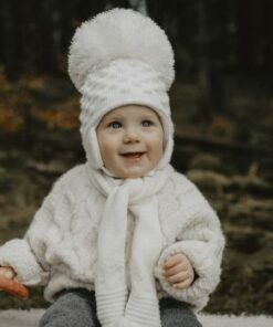 Baby smiling, wearing a large white Satila hat with a huge pom pom at the top.
