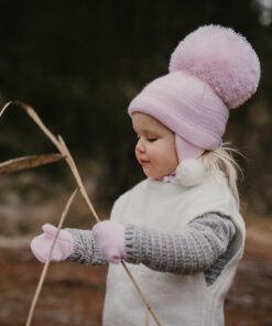 Pink Large Pom Hat from Satila being worn by little girl with white and grey jacket with pink gloves in a forest.